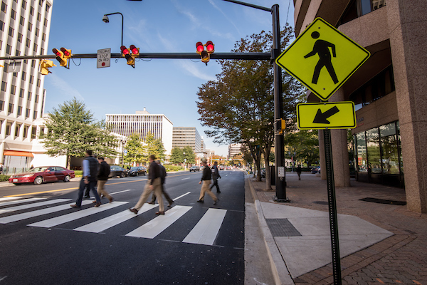 People cross the street on a crosswalk and under a HAWK pedestrian beacon signal.